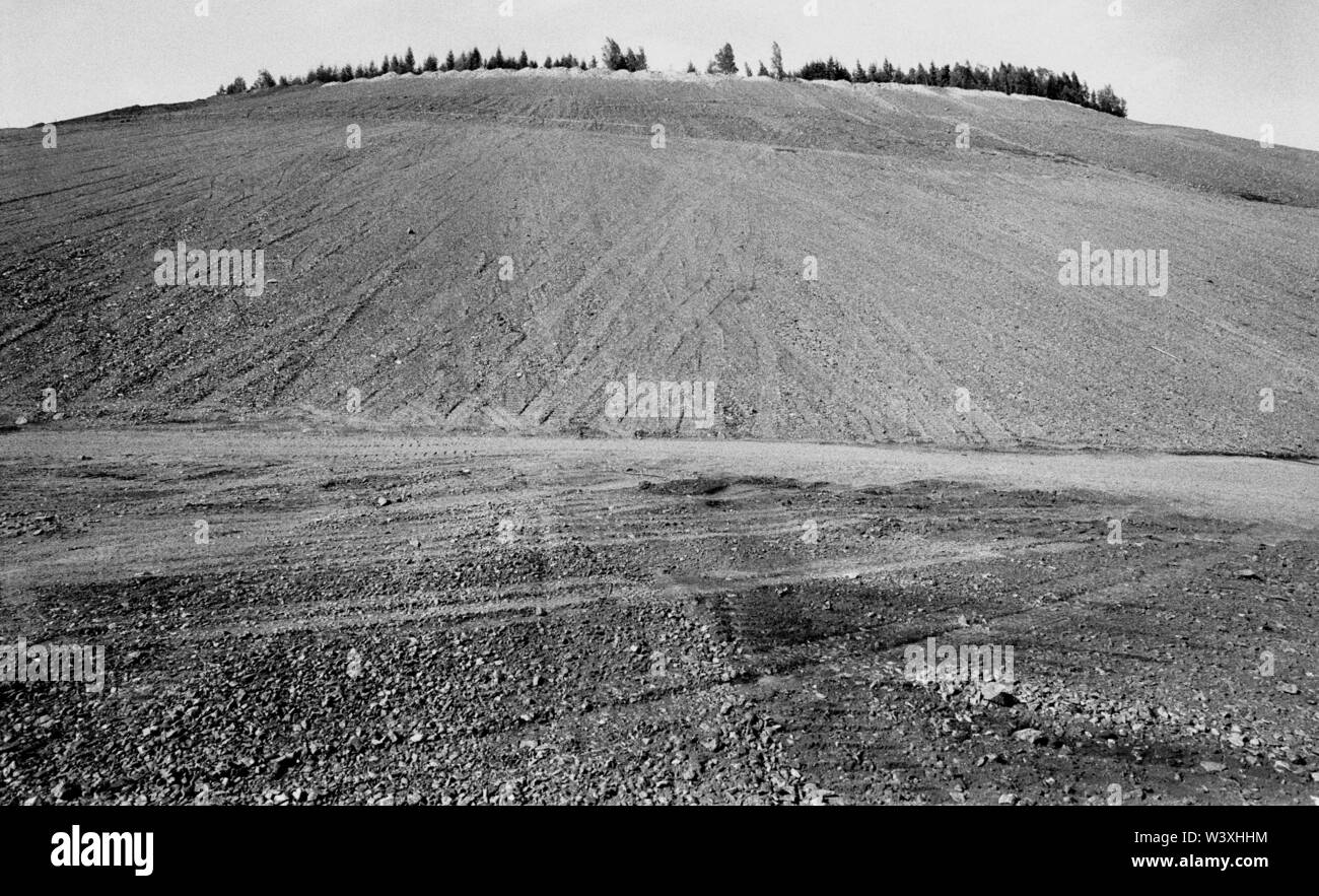 FILED - 01 January 1992, Berlin, Aue: Saxony/GDR/Energy/1992 Uranium dumps in Schlema near Aue, The remediation of major environmental damage has begun. The heap is flattened and terraces are laid out, bushes are planted. Access for the population will not be possible for a very long time. The renovation will be carried out by WISMUT AG. An excavator distributes a mixture of topsoil and ash // Erzgebirge/Environment/Atom/Uranium/Mining The German-Soviet joint stock company was founded after the emergence of the GDR to allow the Soviet Union further access to uranium in the Erzgeb Stock Photo