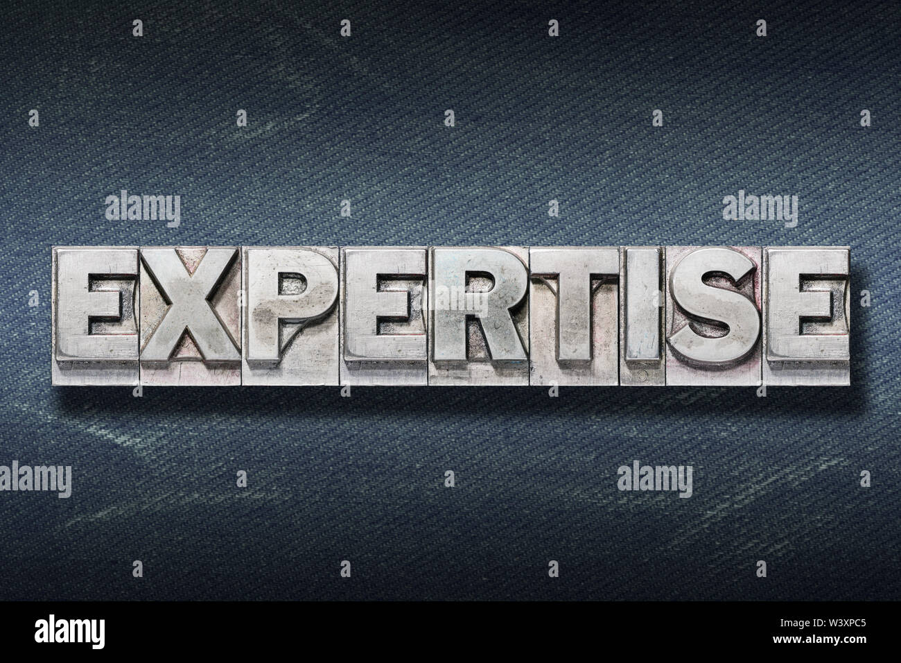 expertise word made from metallic letterpress on dark jeans background Stock Photo