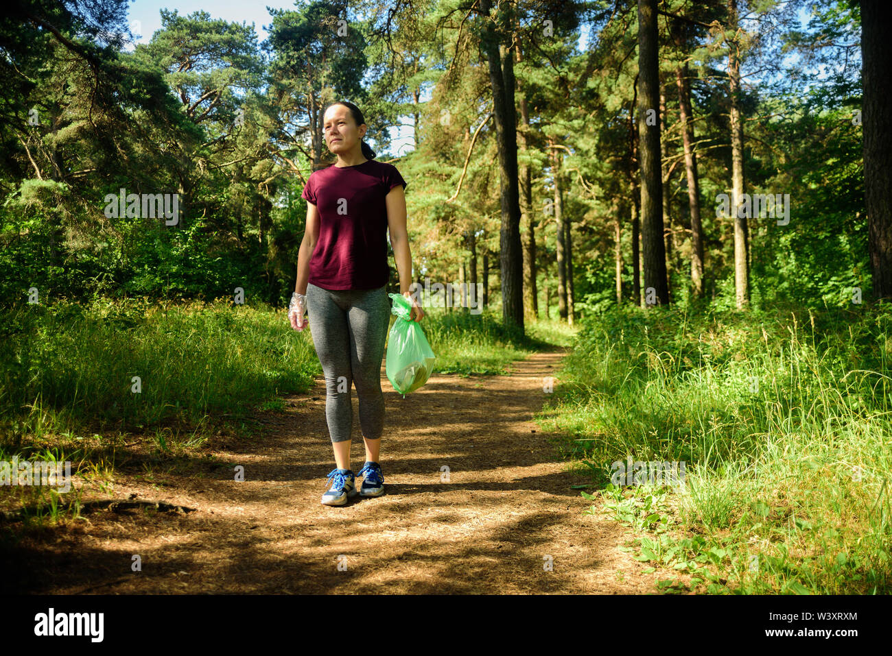 Woman jogging with garbage bag in forest. Collecting trash. Plogging