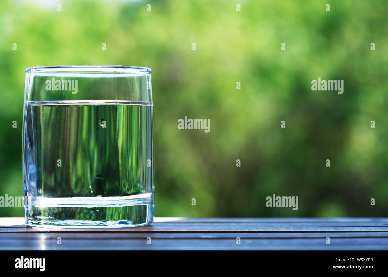 Glass of cold water against nice green nature background Stock Photo - Alamy
