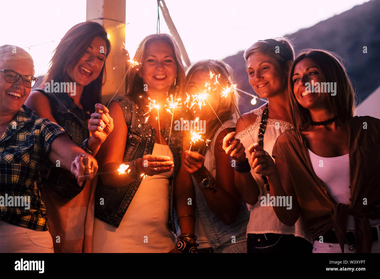 New year eve celebration with group of mixed ages and generations women having fun with sparklers outdoor - people having fun together in friendship - Stock Photo