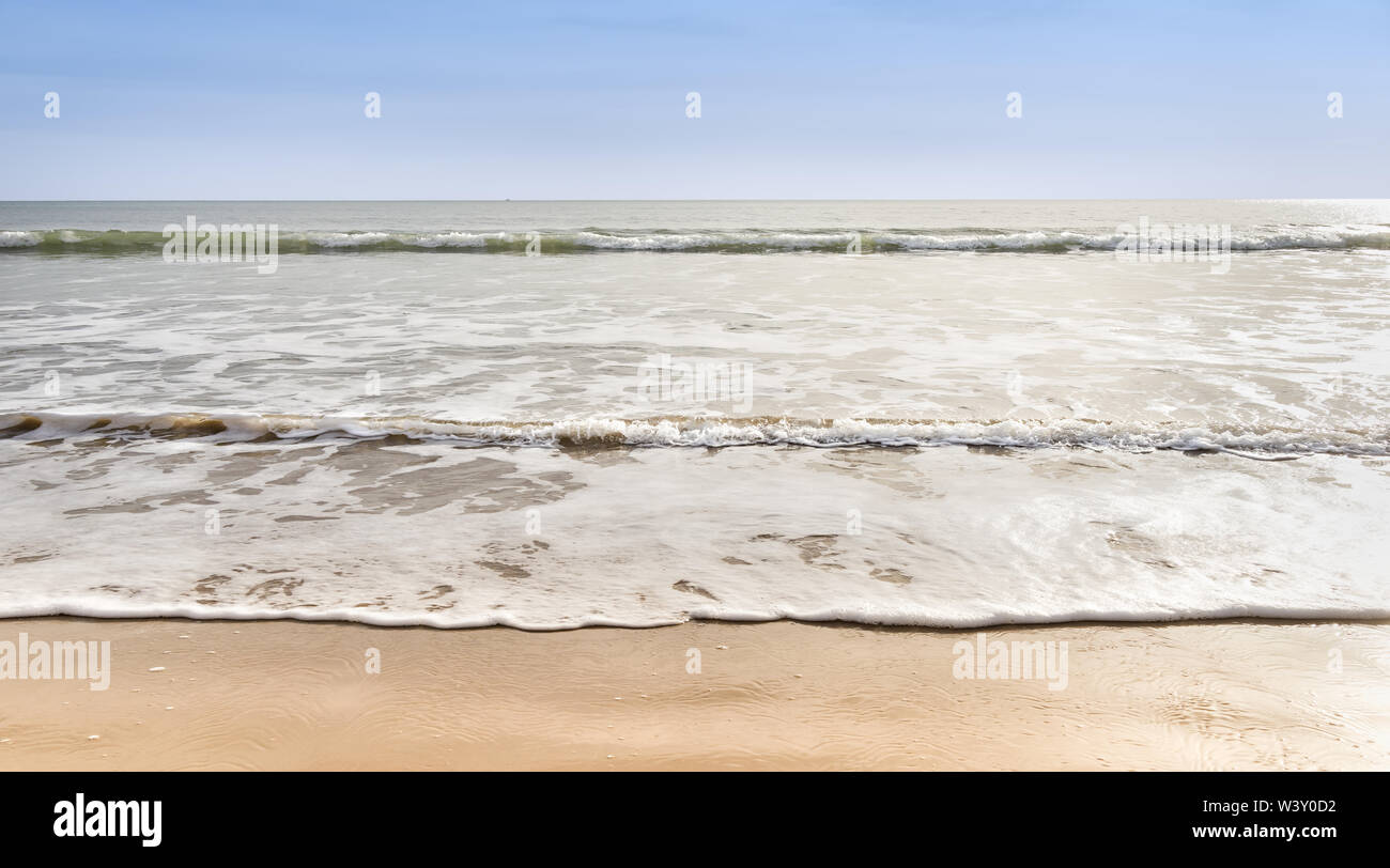 Gently lapping waves on a sandy beach with blue sky Stock Photo