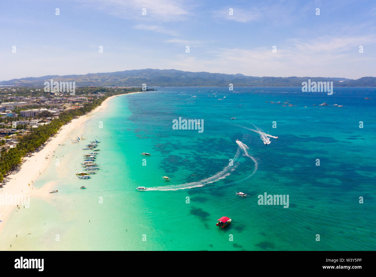 Seascape in the Philippines in sunny weather, view from above. Transparent sea and tourist boats near the island of Boracay. Residential buildings and hotels on the big island. Stock Photo