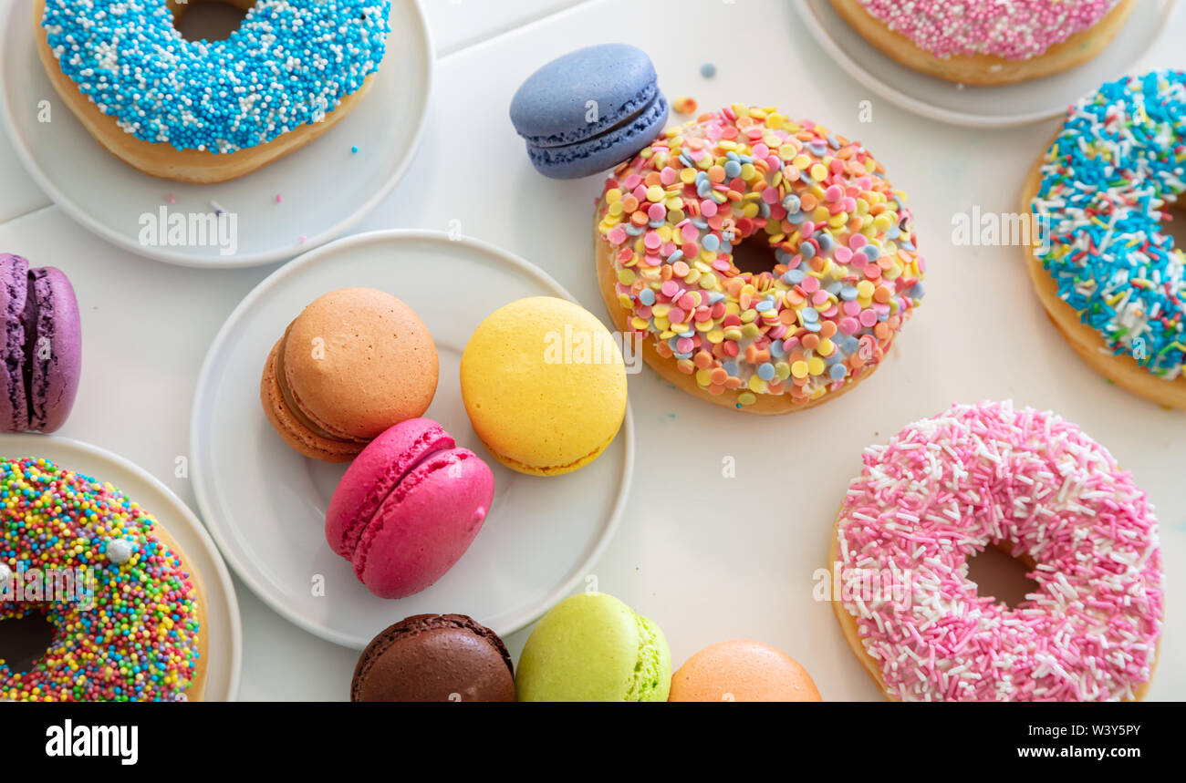 Donuts and french macarons on white table, close up view with details, top view Stock Photo