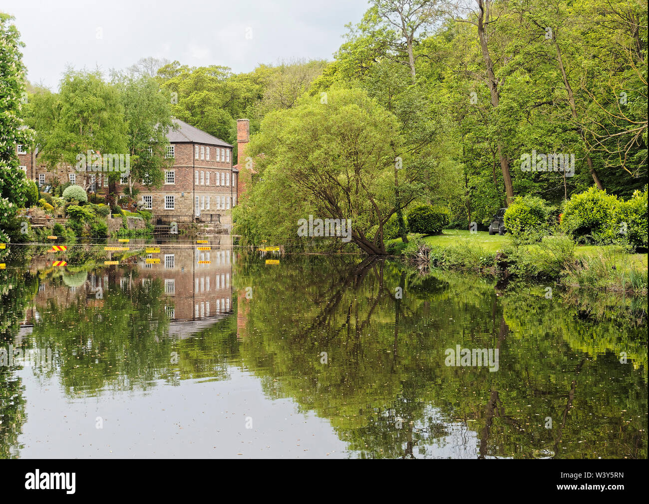 Looking downstream along the River Nidd in Knaresborough, North Yorkshire towards a weir and a former mill now converted into a house. Stock Photo
