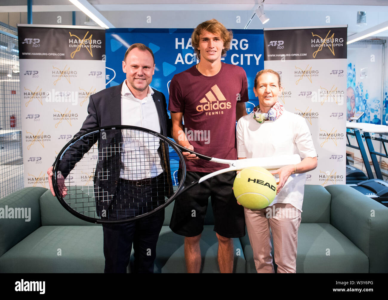Hamburg, Germany. 18th July, 2019. Andy Grote (SPD, sports senator of  Hamburg, l), Alexander Zverev, tennis player from Germany, and Sandra  Reichel, tournament director, hold an oversized tennis racket during a press