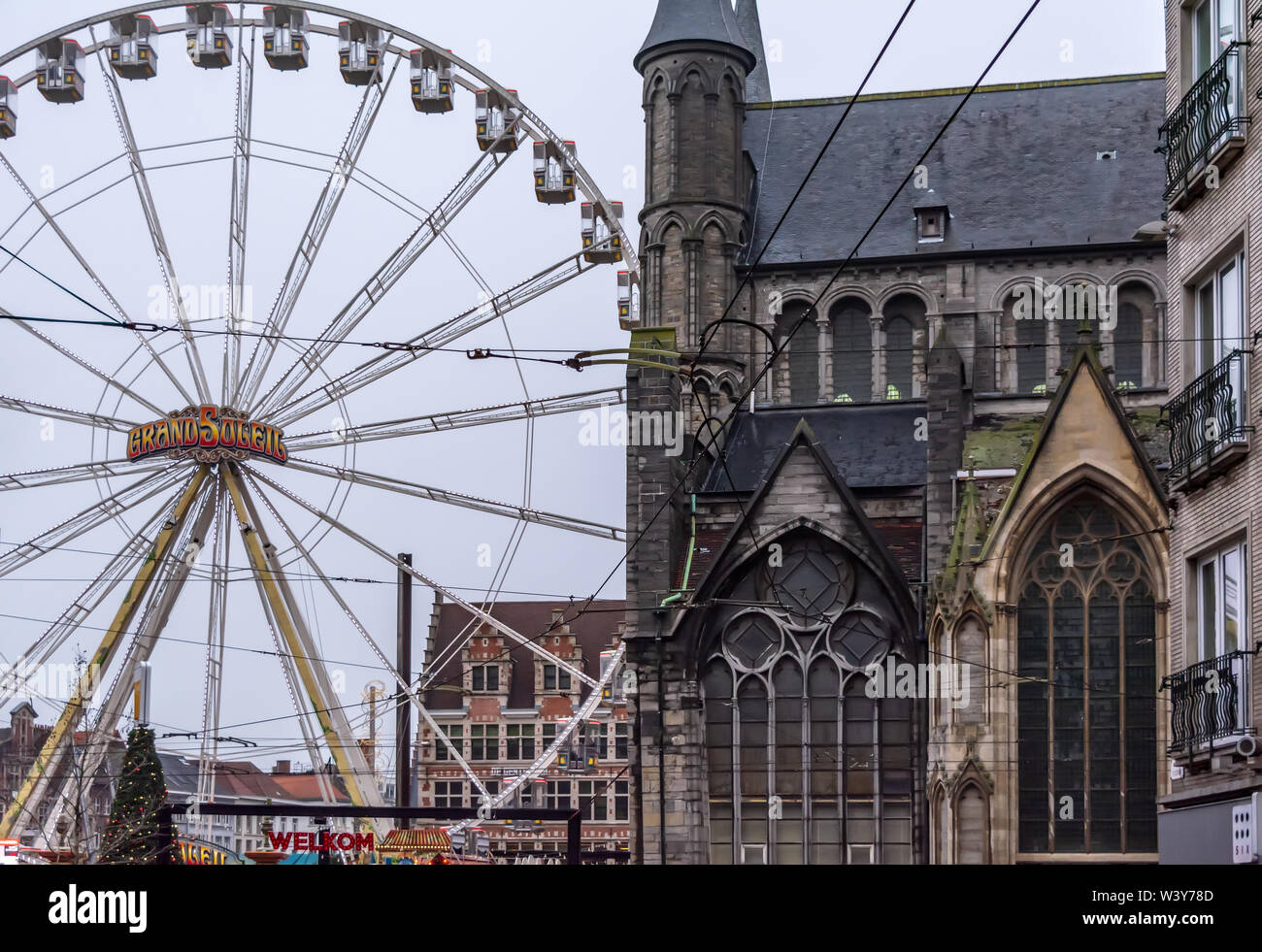 Ferris wheel and Christmas market in the city center near gothic Saint Nicholas' Church (Sint-Niklaaskerk) in in foggy winter morning. Stock Photo