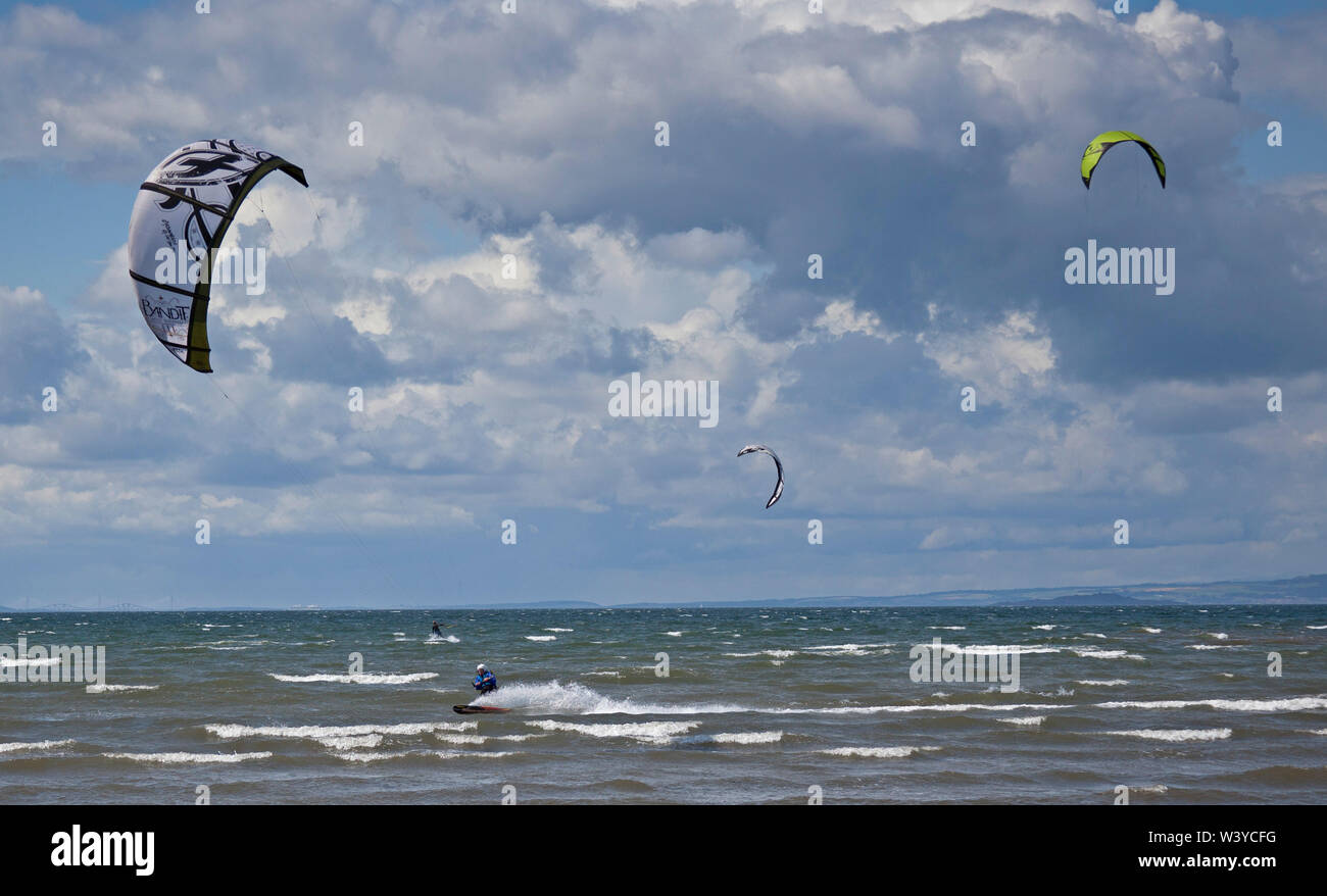 Longniddry Bents, East Lothian, Scotland. UK. 18th July 2019. Kitesurfers make the best of the sunny and windy but changeable conditions with 27km/h winds and potential gusts of 49 km/h, great skill was demonstrated as they passed close by each other without their kites becoming tangled up. Stock Photo