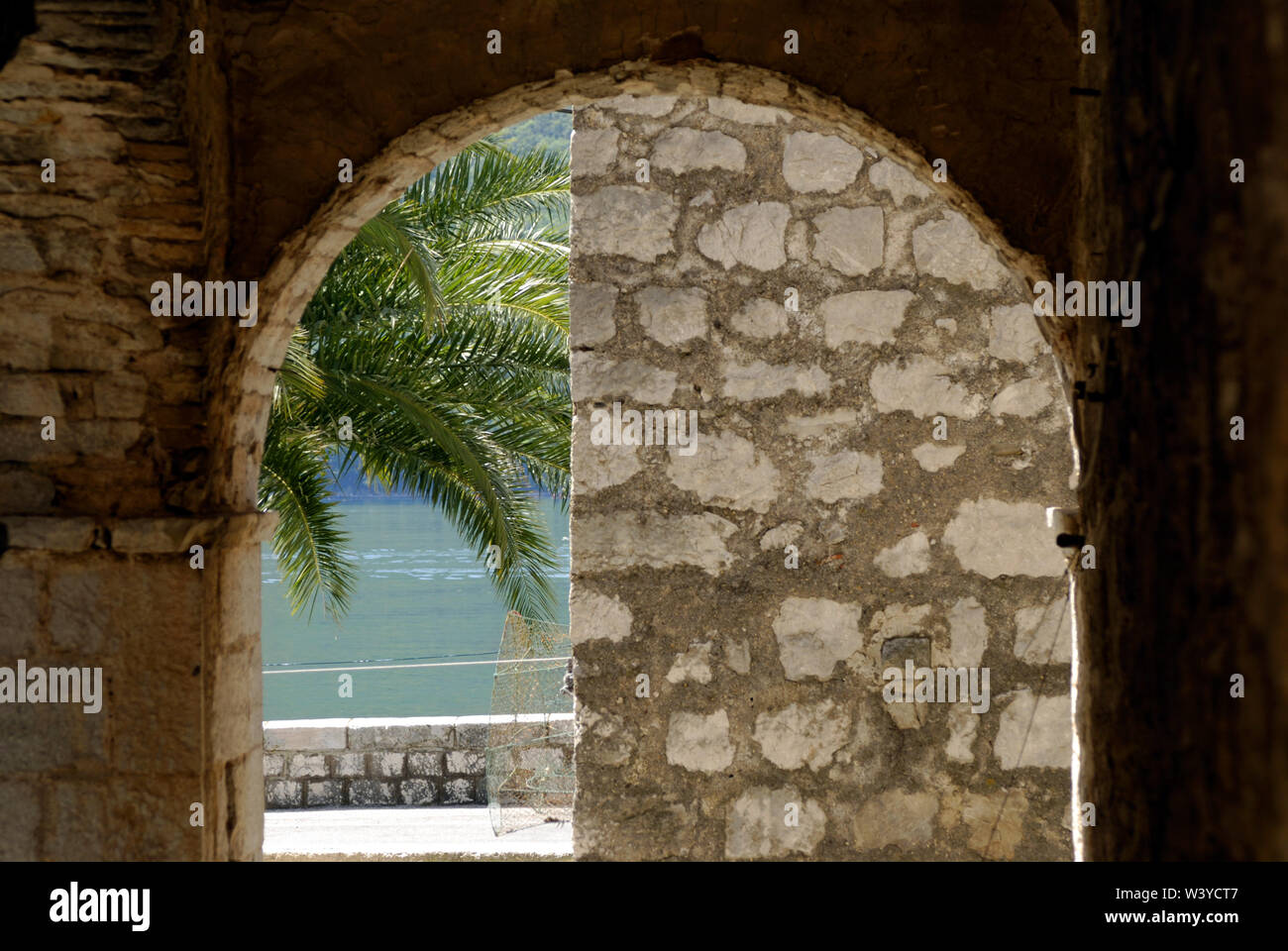 Palm tree and water view trough old stone arch. Montenegro Stock Photo