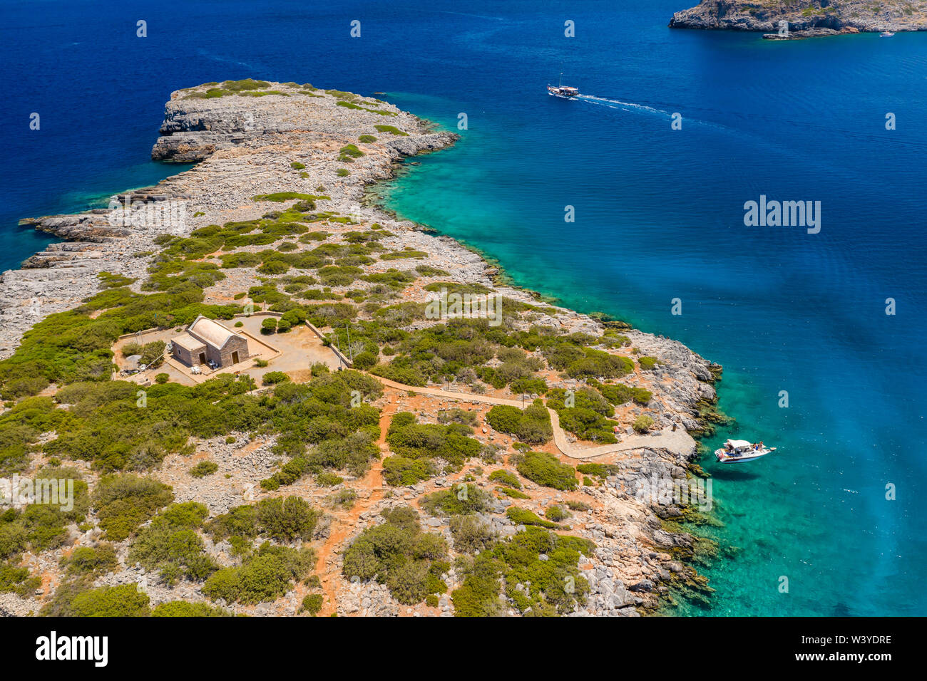 Aerial drone view of a warm, blue, clear ocean with dry coastline and boats (Kolokitha Island, Elounda, Crete) Stock Photo