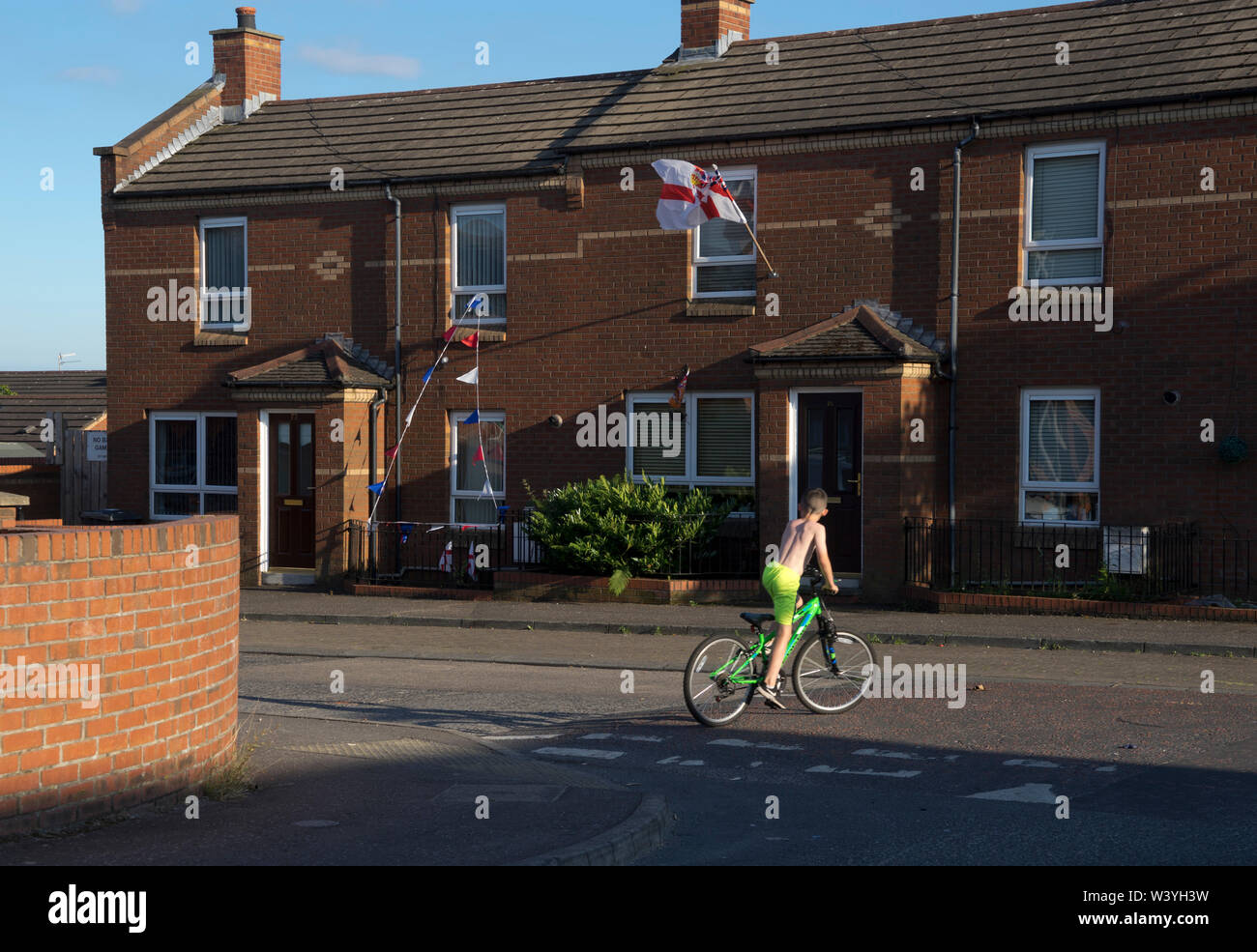Child on a bicycle with loyalist flags and banners in background in the Shankhill area of Belfast ,Northern Ireland Stock Photo