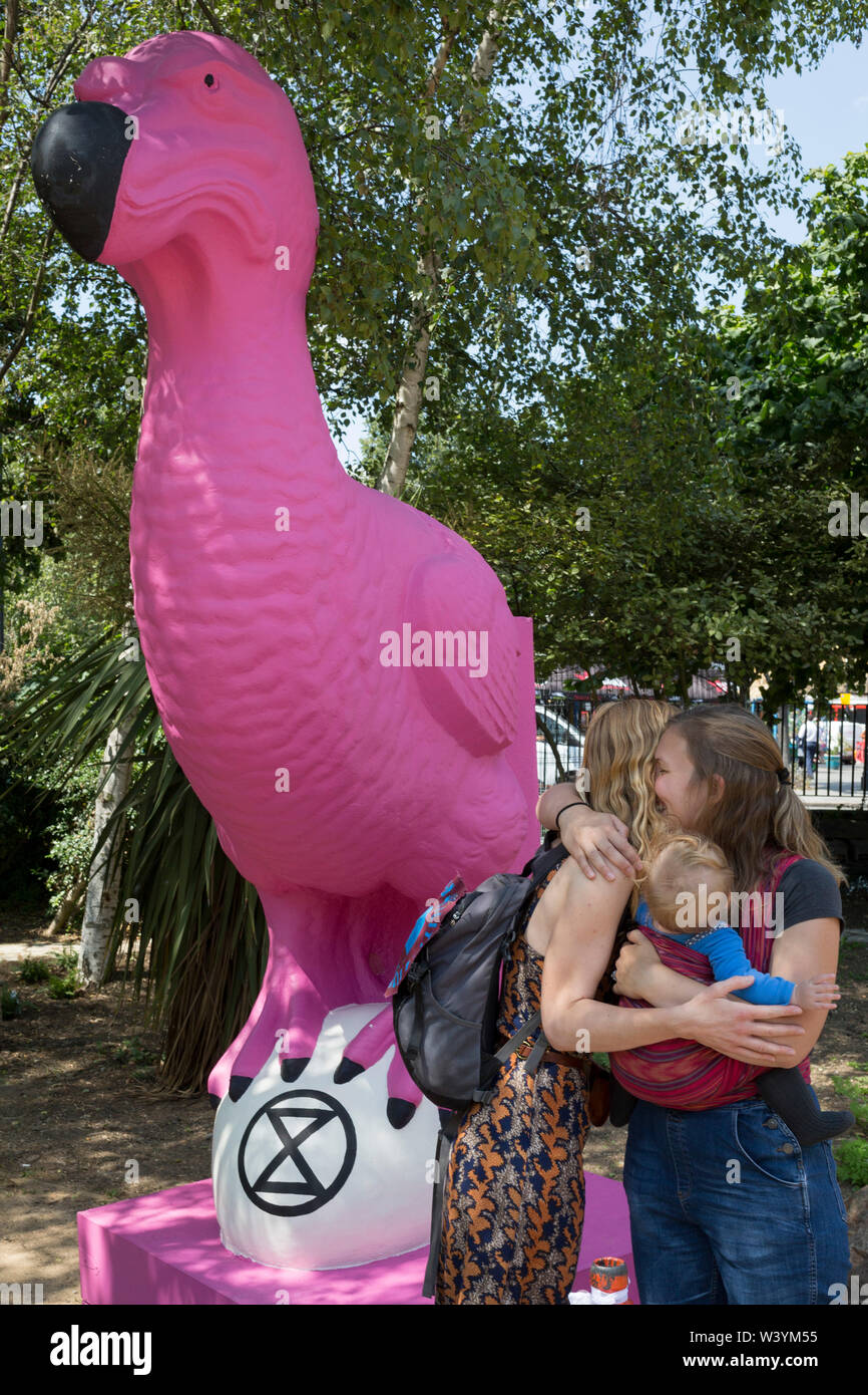 Two women friends hug next to an extinct pink Dodo which stands in the makeshift climate change protest camp on Waterloo Millennium Green, during the week-long, country-wide protest by environmental campaigners, Extinction Rebellion, on 16th July 2019, in London, England. The five-day 'summer uprising's message is for the UK government to outlaw what protesters call 'Ecocide'. Stock Photo