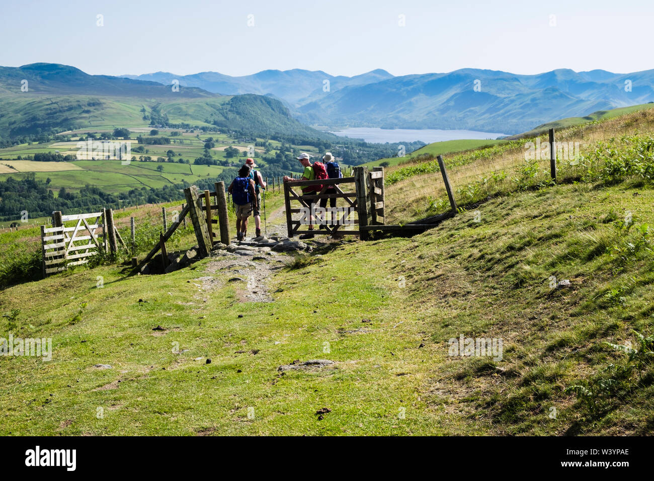 Hikers hiking and closing a gate on Cumbria Way trail on Lonscale Fell hillside in Lake District National Park. Keswick, Cumbria, England, UK, Britain Stock Photo
