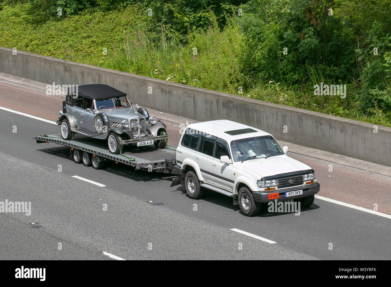 1992 90s silver Beauford being towed on a trailer by a 1997 Toyota  Landcruiser Amazon GX; UK Vehicular traffic, transport, modern, saloon cars,  south-bound on the 3 lane M6 motorway highway Stock