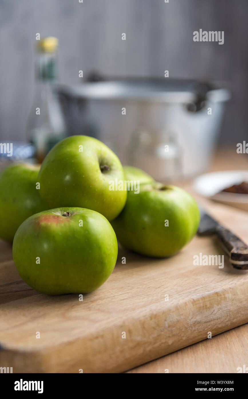 Bramley apples on wooden board with preserving pan in background. Stock Photo