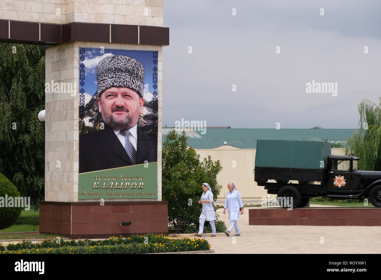 Chechen Women walk past a large photo bearing the image of Akhmad Kadyrov former Head of the Chechen Republic placed at the Memorial complex of glory named after Akhmat-Khadji Kadyrov in Grozny the capital city of Chechnya in the North Caucasian Federal District of Russia. Stock Photo
