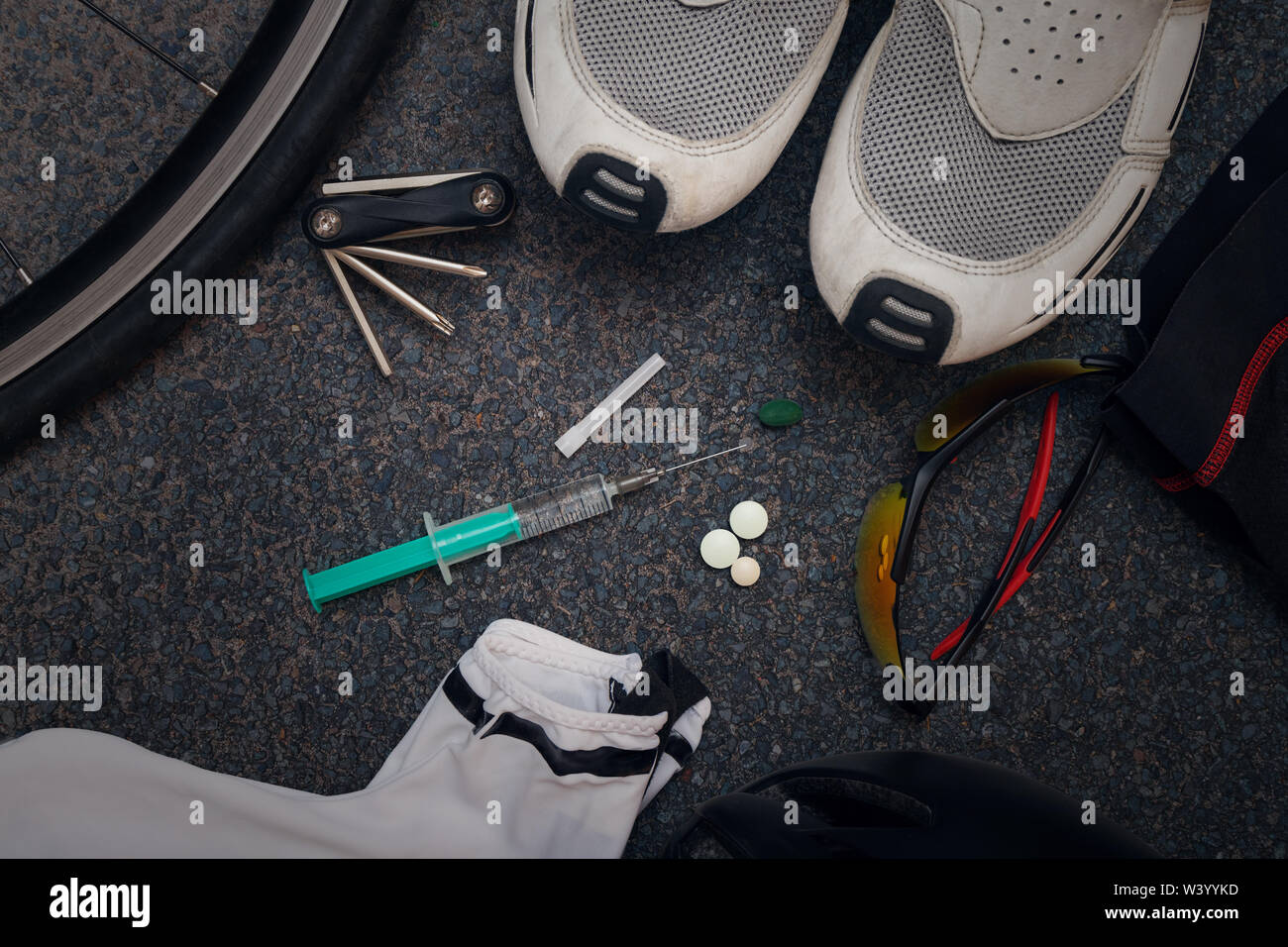 Cycling clothing and bike equipment on asphalt with a syringe and tablets in the middle, illustrating doping or the abuse of performance enhancing substances in amateur and professional sport. Stock Photo