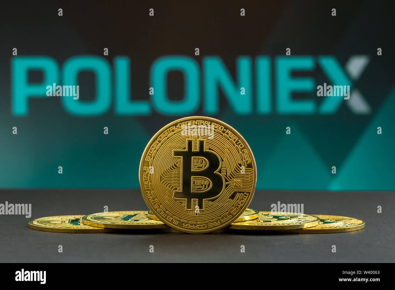 A big Bitcoin cryptocurrency coin in the centre and other bitcoin coins from both side in front of Poloniex crypto market . The pyramid of bitcoin Stock Photo