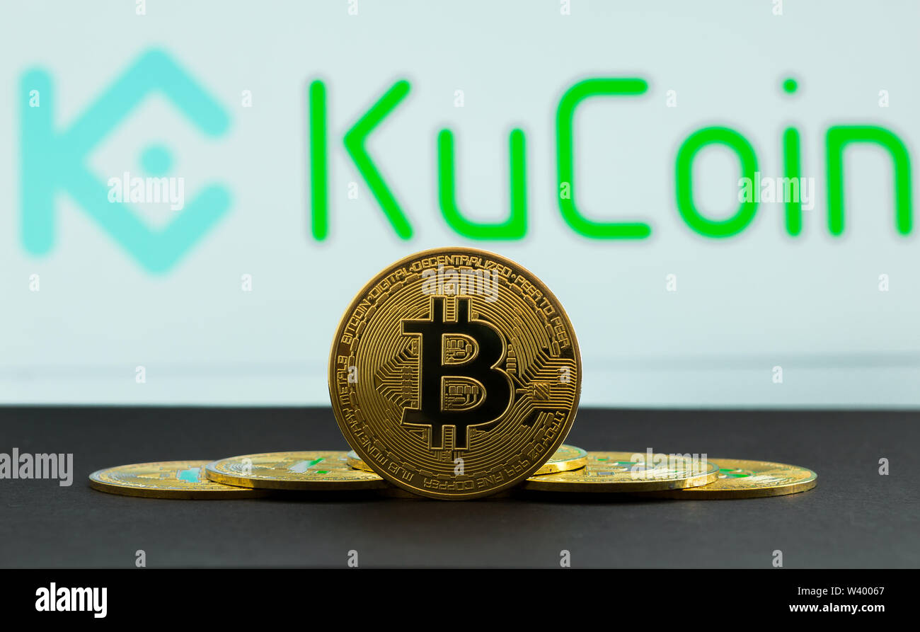 The coins of bitcoin are in front of logo of Ku Coin crypto stock exchange background. In the foreground is a BTC coins and on the background is a Stock Photo