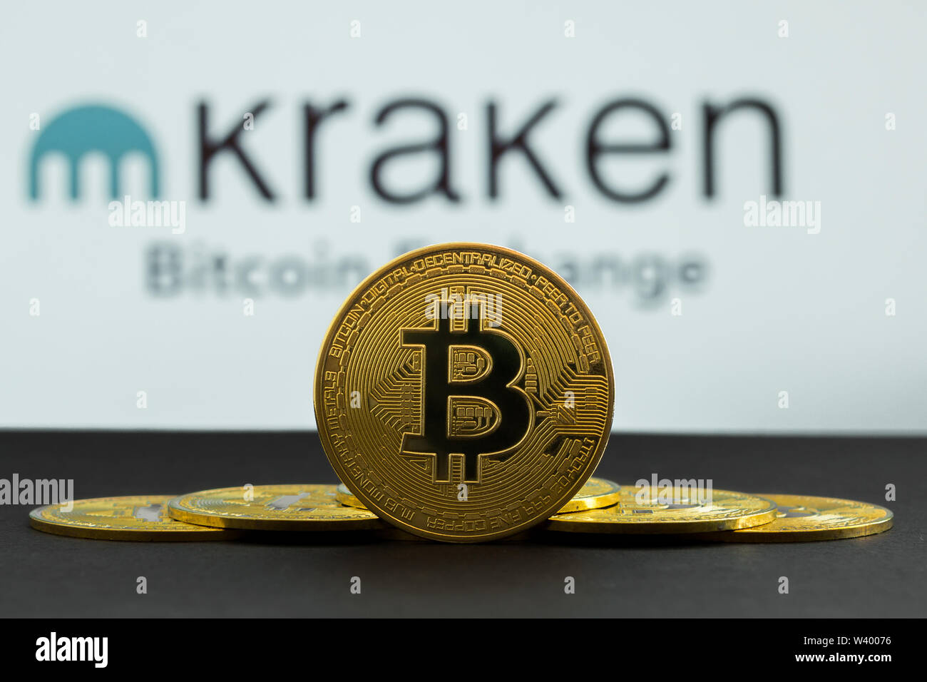 The coins of bitcoin are in front of logo of Kraken crypto stock exchange background. In the foreground is a BTC coins and on the background is a Stock Photo