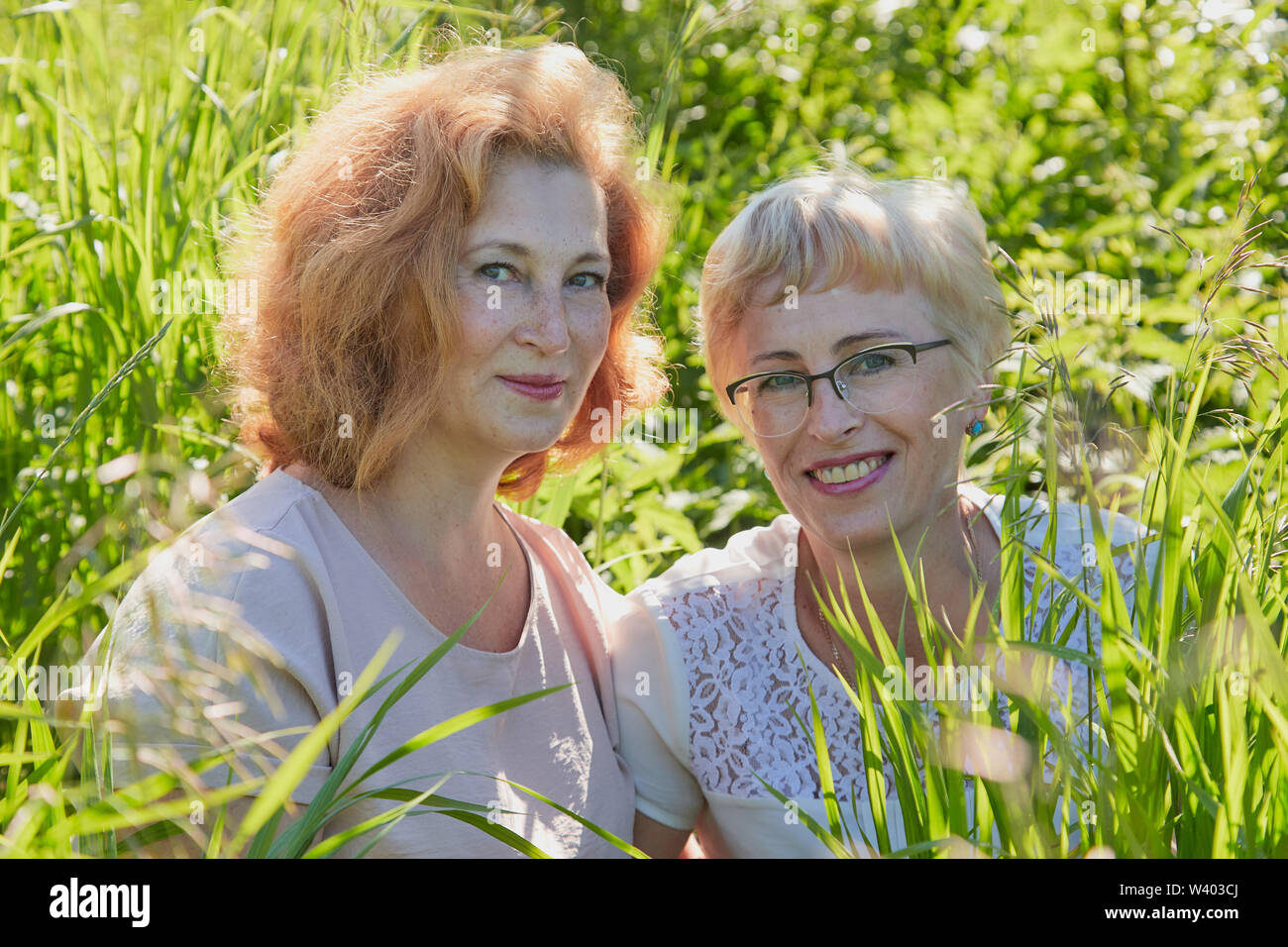 Two female friends having fun on nature. Chubby and slim middle-aged women pensioners in a green field Stock Photo