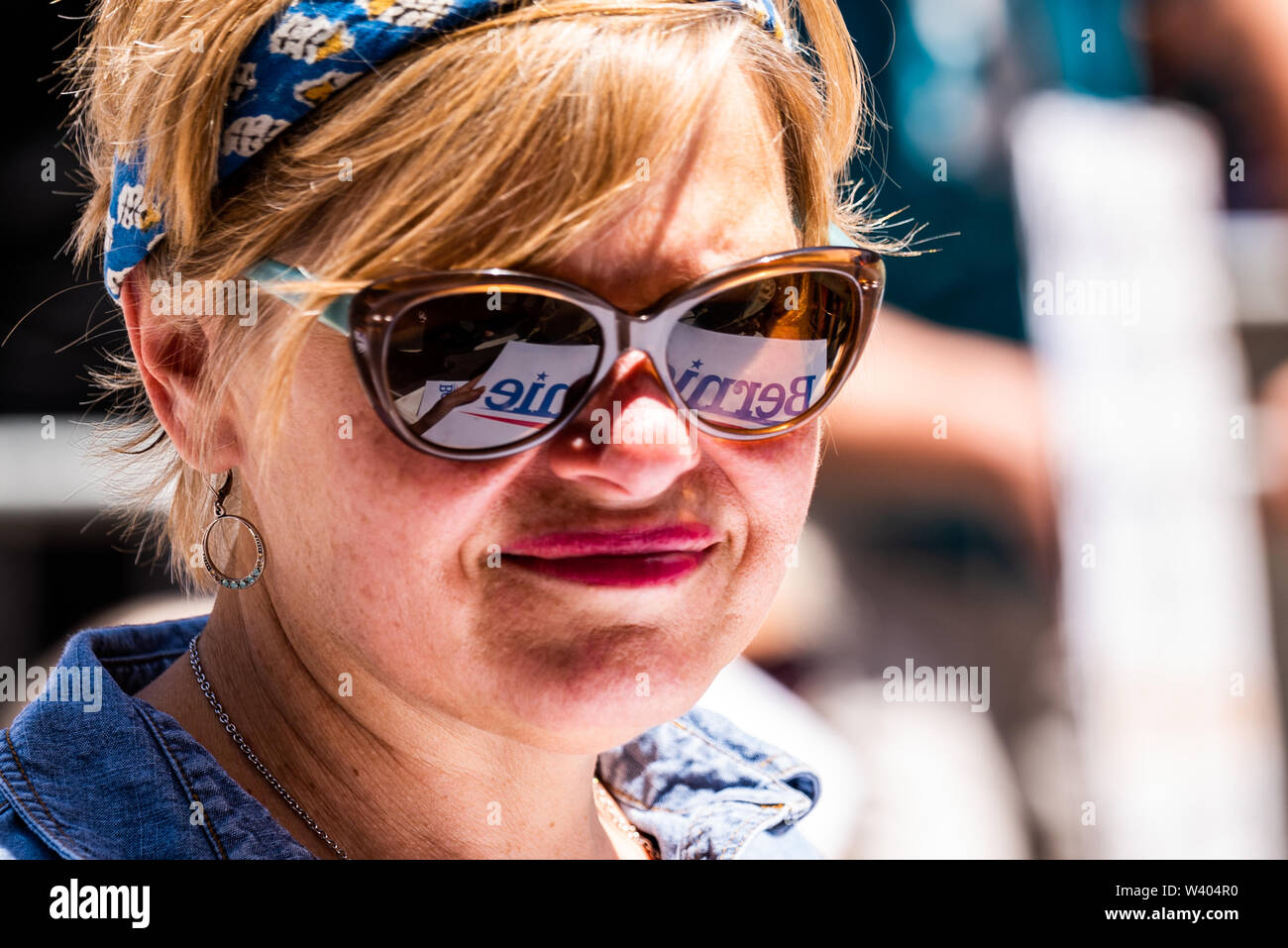 Philadelphia, Pennsylvania / USA. A political sign for Bernie Sanders is reflected in the glasses of a woman attending a rally in front of Hahnemann University Hospital. July 15, 2019. Photo Credit: Chris Baker Evens. Stock Photo