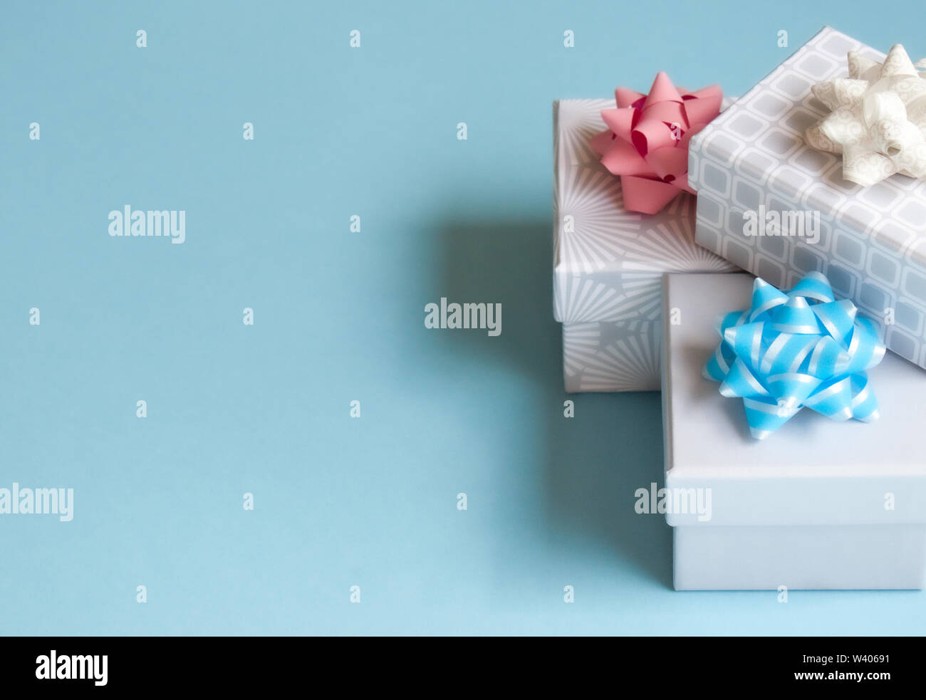 Three light gray gift boxes with light bow on blue background. Festive concept. Stock Photo