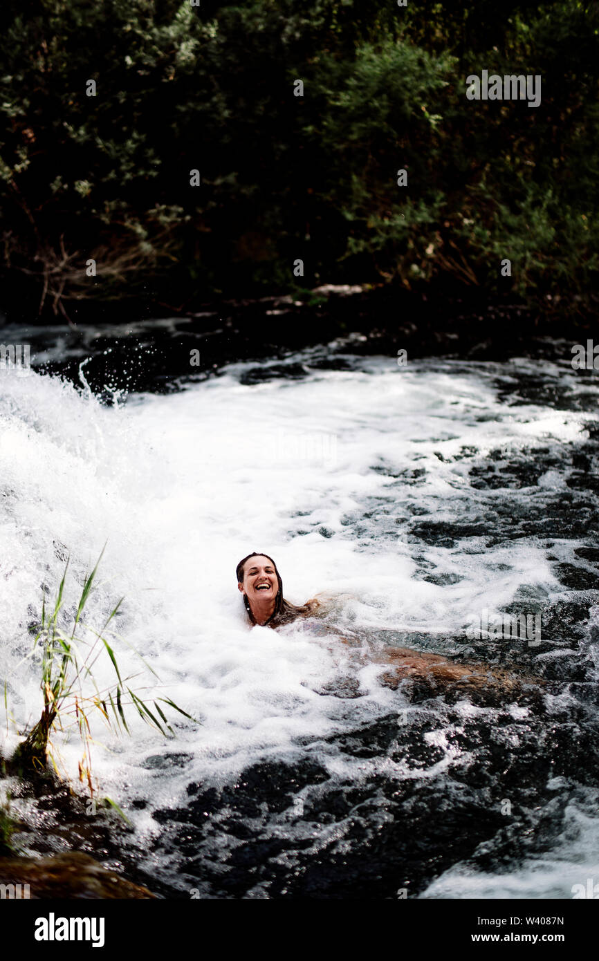 Blond woman bathing in beautiful river waterfall. Stock Photo