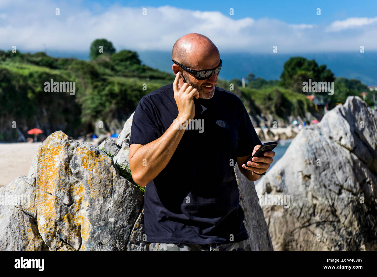 bald man on beach using headphones and mobile phone Stock Photo