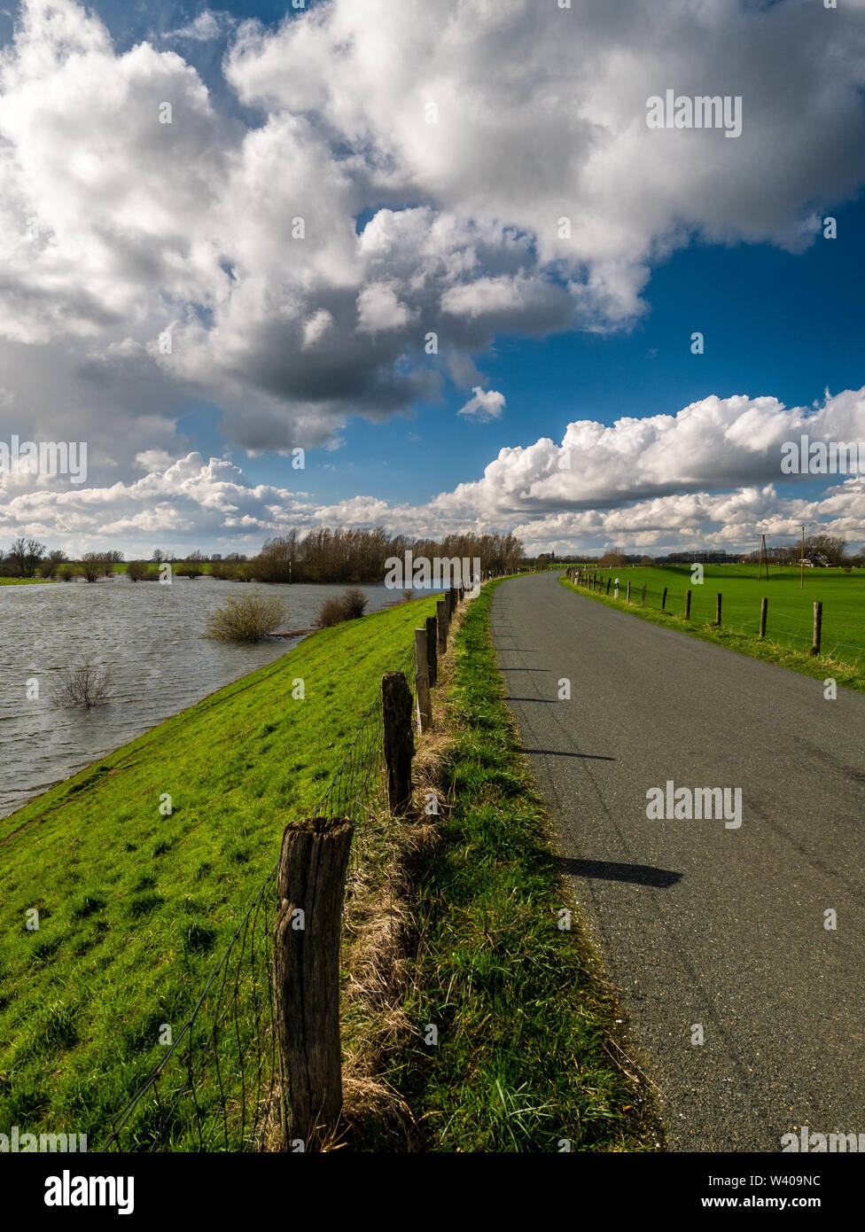 Small road on grass covered dyke under white clouds Stock Photo