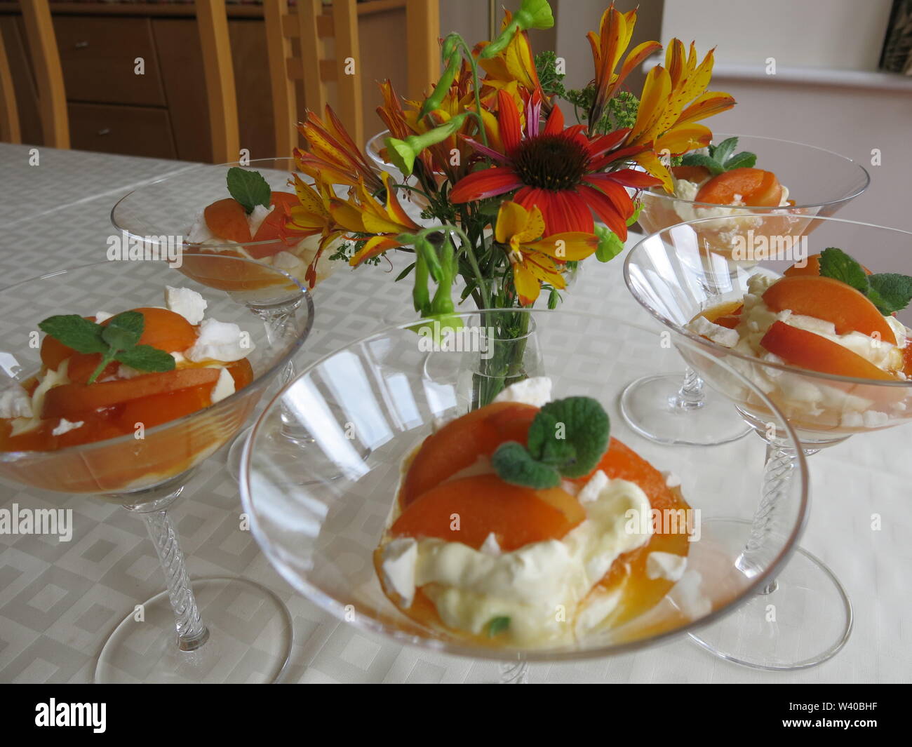 Array of dessert glasses arranged round a small vase of flowers for summer dining; apricot, white chocolate & whipped cream fool garnished with mint. Stock Photo