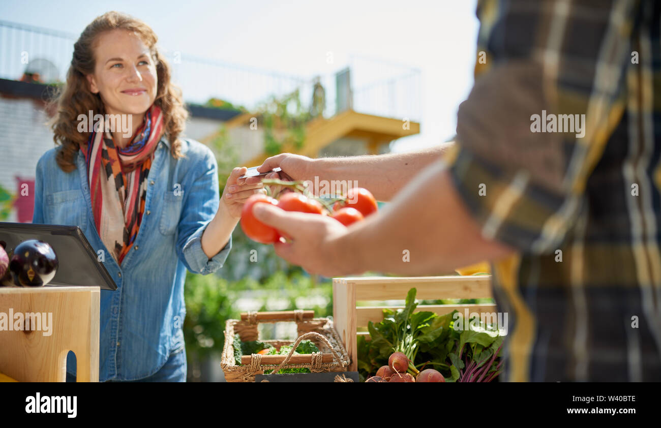 Friendly woman tending an organic vegetable stall at a farmer's market ...