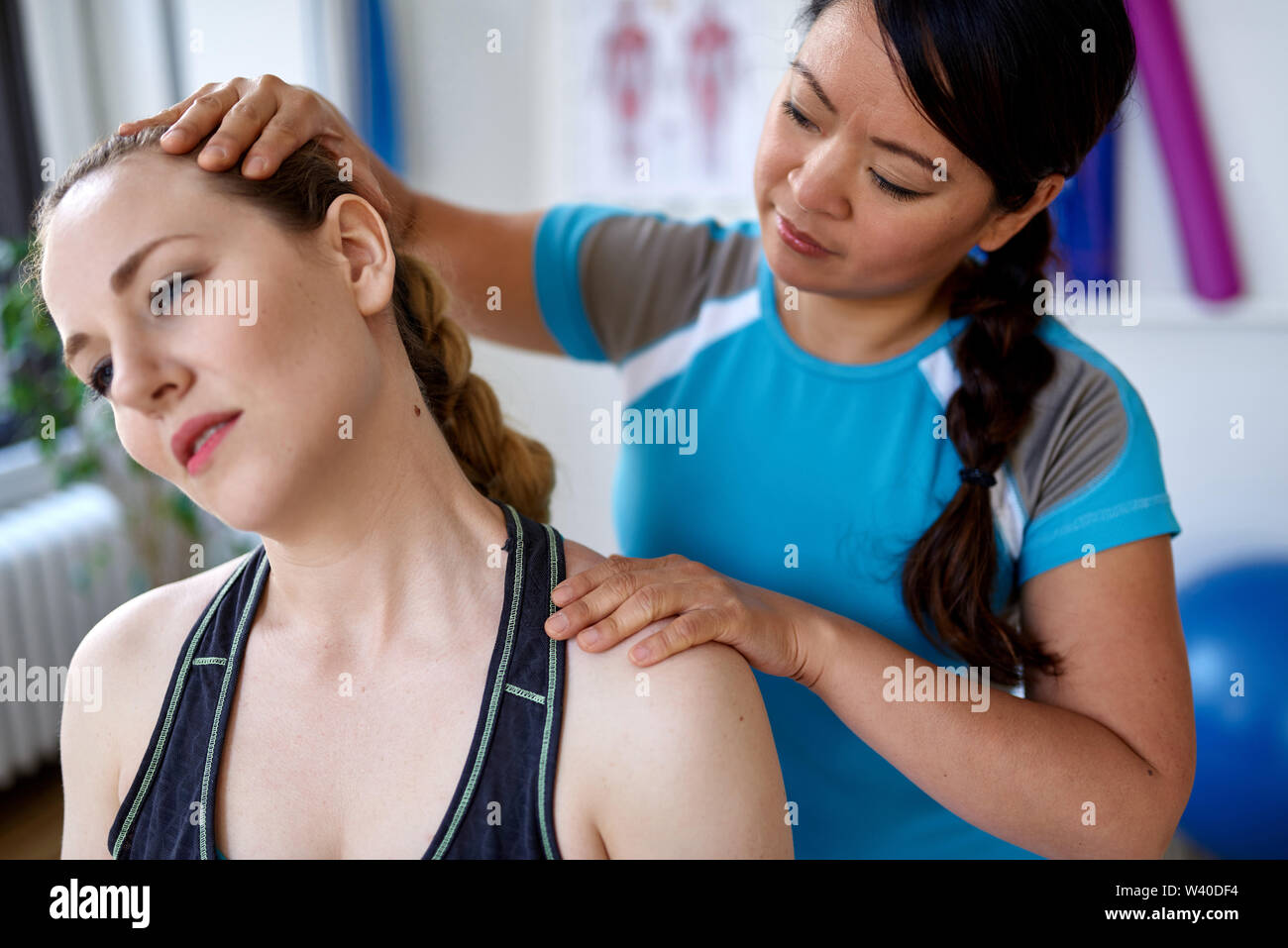 Chinese woman physiotherapy professional giving a treatment to an attractive blond client in a bright medical office Stock Photo