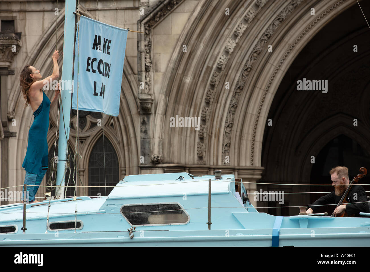 London, UK. 15th July 2019. Extinction Rebellion activist raising the 'make ecocide law' flag at the climate action group's protest in front of the Royal Courts of Law on the Strand, London. Credit: Joe Kuis / Alamy News Stock Photo