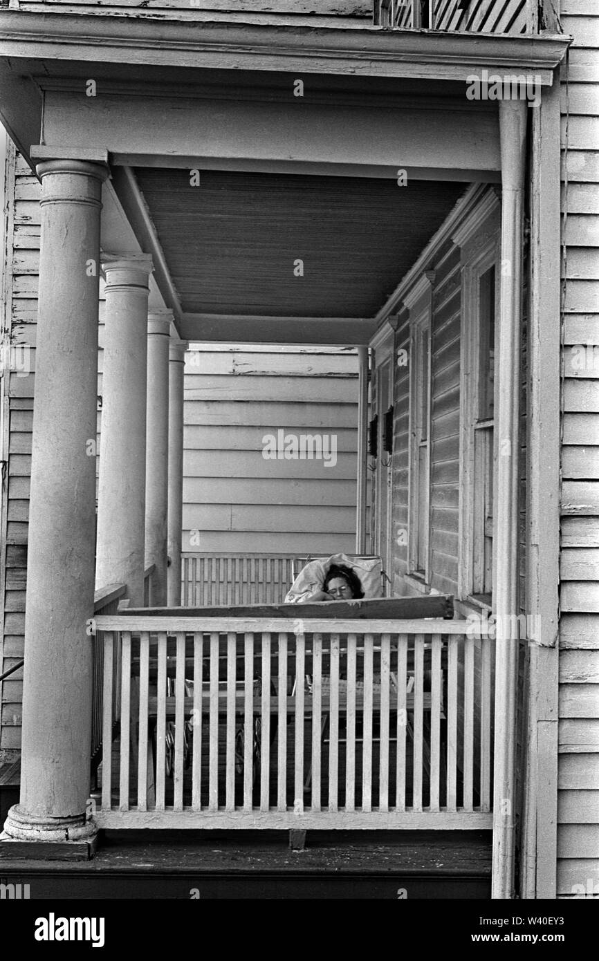 Old timber clad home painted white, wood cladding, wooden boards, exterior of building. A woman is asleep sleeping on her house porch. New Brunswick, New Jersey. 1969, USA 60s US HOMER SYKES Stock Photo