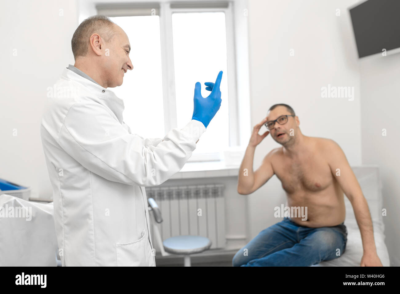 Doctor urologist puts a medical glove on the arm to examine the patient's prostate, prostate massage, lymphatic drainage. Stock Photo