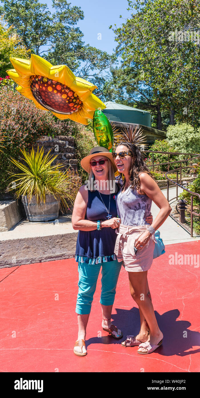 Two female Millennials celebrate one of their birthdays with a huge sun shaped mylar balloon on the patio at the Nepenthe restaurant on highway 1. Stock Photo