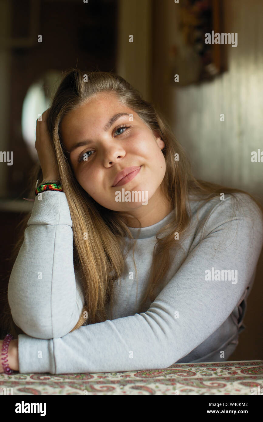 Portrait of teenage girl with long hair sitting at the table in his ...