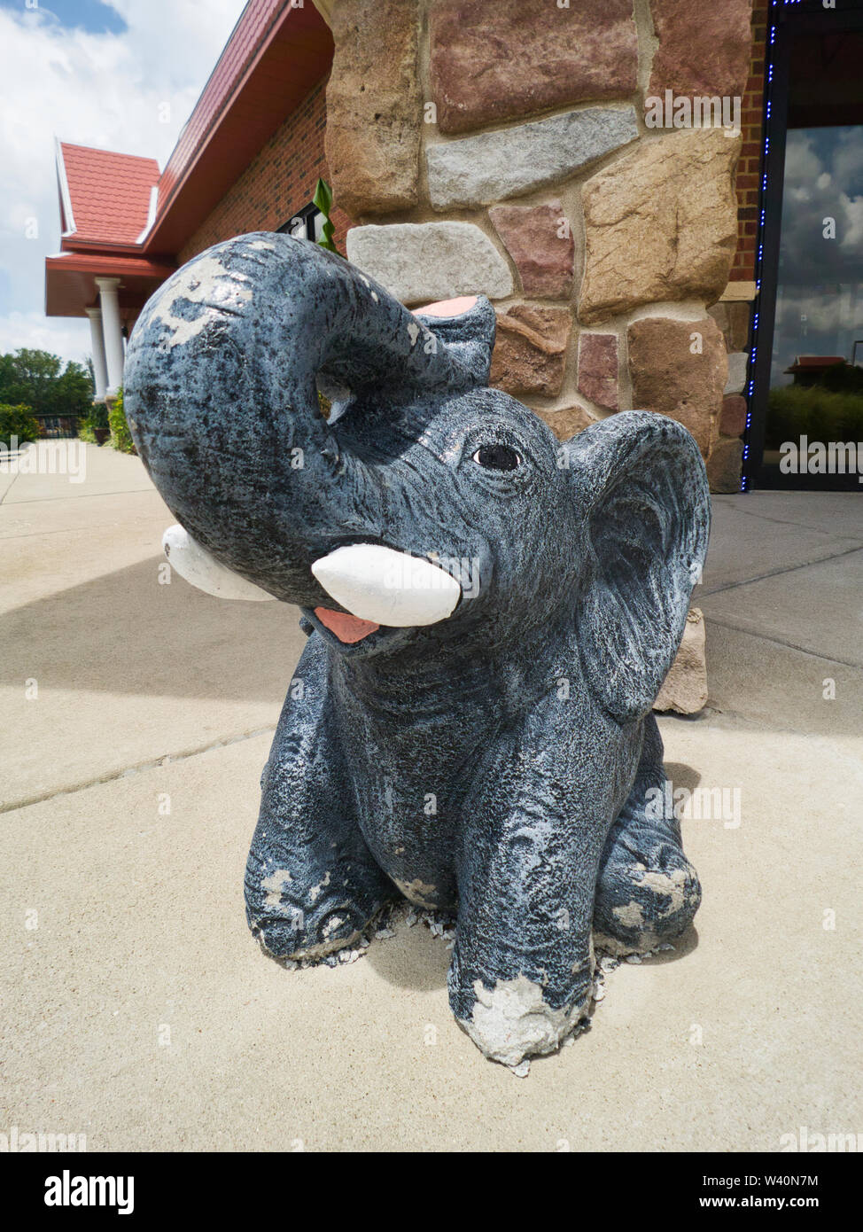 Happy grey elephant statue outside of thai restaurant. The elephant has a smile on his face and his trunk in the air. Wide angle closeup. The statue i Stock Photo