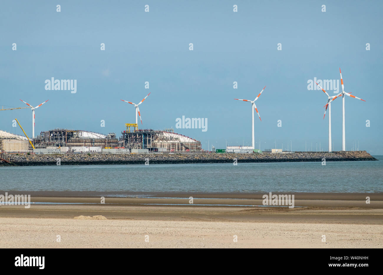 Zeebrugge, Flanders, Belgium -  June 18, 2019: Closeup of LNG terminal in port of Zeebrugge under blue sky as seen from beach in Knokke-Heist. Windmil Stock Photo