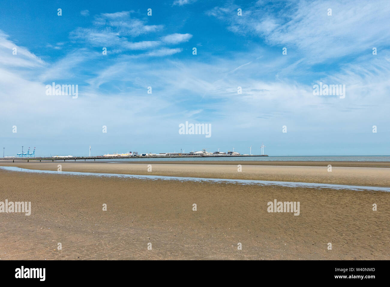 Zeebrugge, Flanders, Belgium -  June 18, 2019: Long shot on LNG terminal in port of Zeebrugge under blue sky with white stripes as seen from beach in Stock Photo