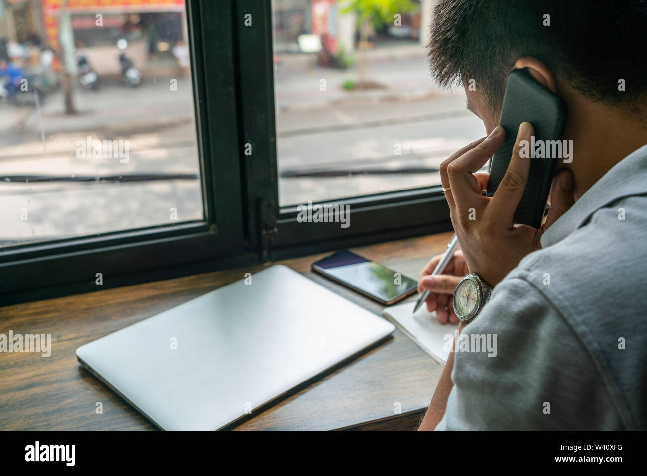 Asian man talking on cellphone and taking notes on table Stock Photo