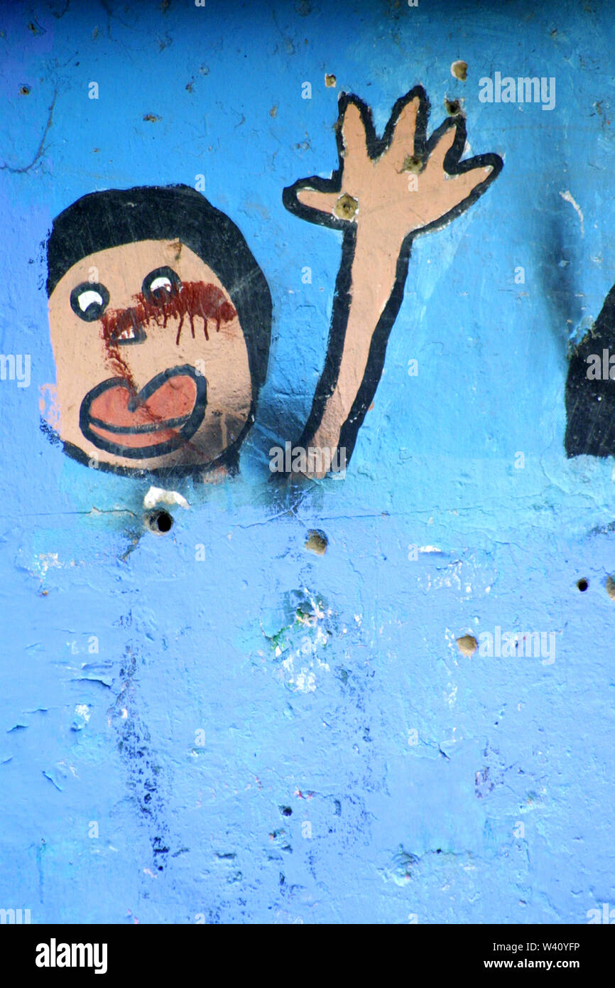 Bullet holes and blood in a blue wall painted with a mural of a boy saluting in Los Erasos, Caracas, Venezuela Stock Photo