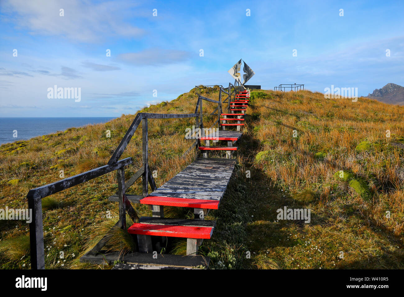 Wooden pathway on Cape Horn island in Chile, leading up to the Cape Horn Memorial Monument on a sunny day. Stock Photo
