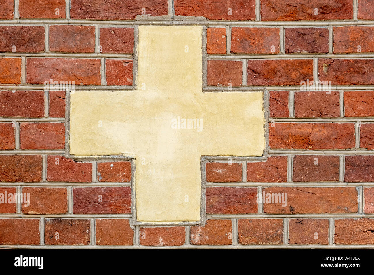 Red brick wall with white-yellowish cross sign background Stock Photo