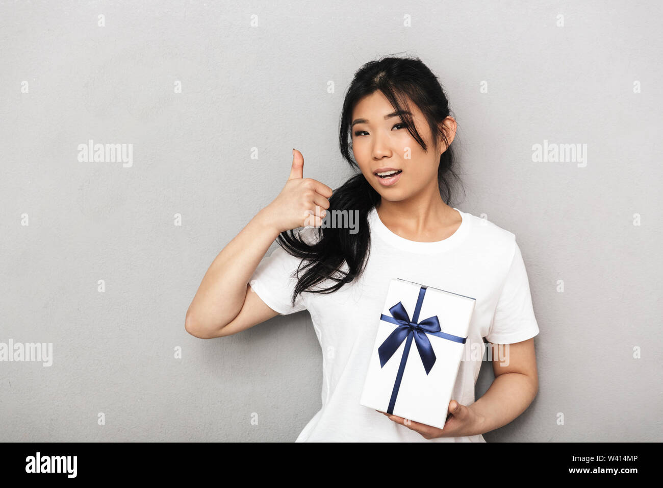 Photo of asian beautiful young woman posing isolated over grey wall ...