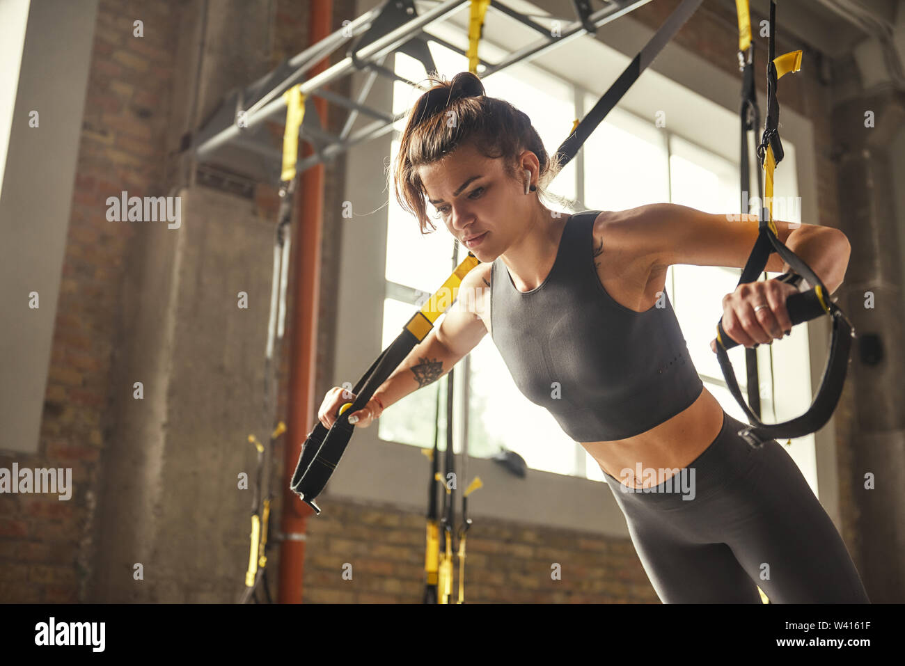 Perfect push-up. Side view of young athletic woman with perfect body in sportswear doing push ups with trx fitness straps in the gym. Professional sport. TRX Training. Workout Stock Photo