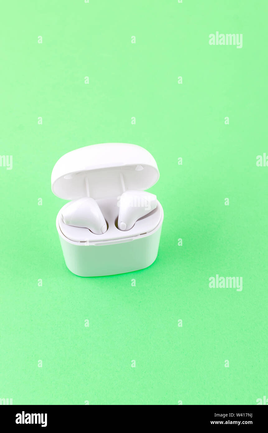 New AirPods wireless Bluetooth entangled 3.5 headphones into the open charging case for Airpods for smartphone and a green background. Copy Space Zapo Stock Photo