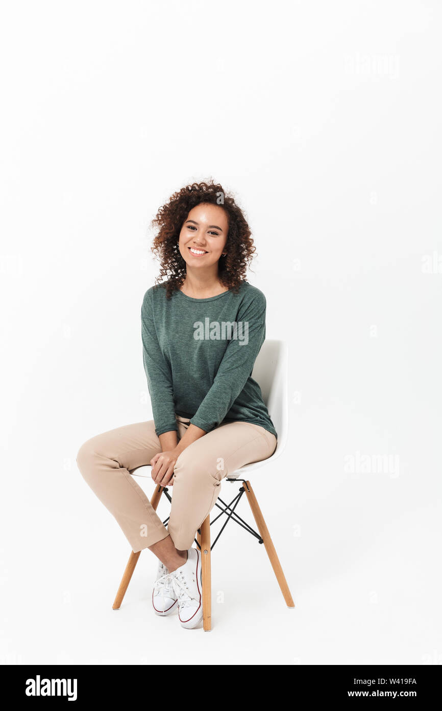 Attractive young african woman sitting on a chair isolated over white ...
