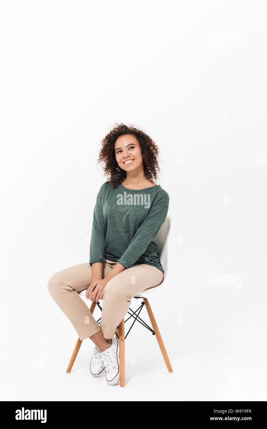 Attractive young african woman sitting on a chair isolated over white ...